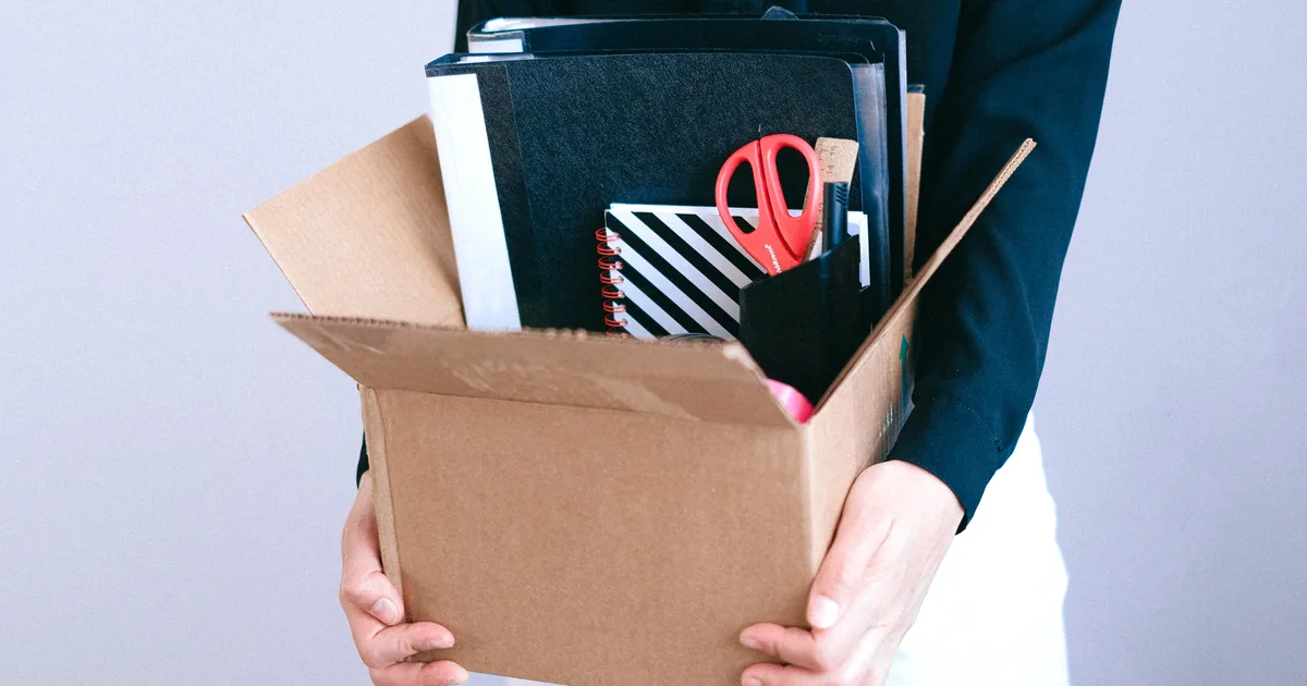 An employee carrying a cardboard box of personal belongings out of the office on their last working day