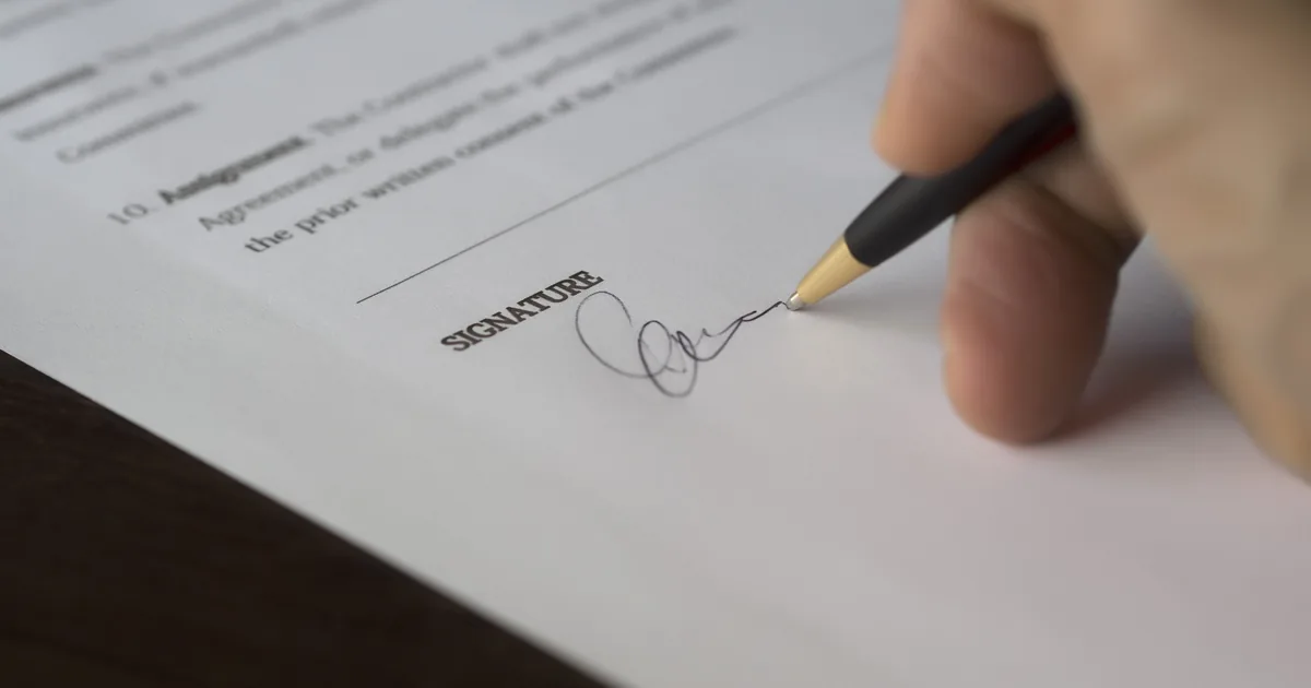 A hand signing on the signature line of an agreement
